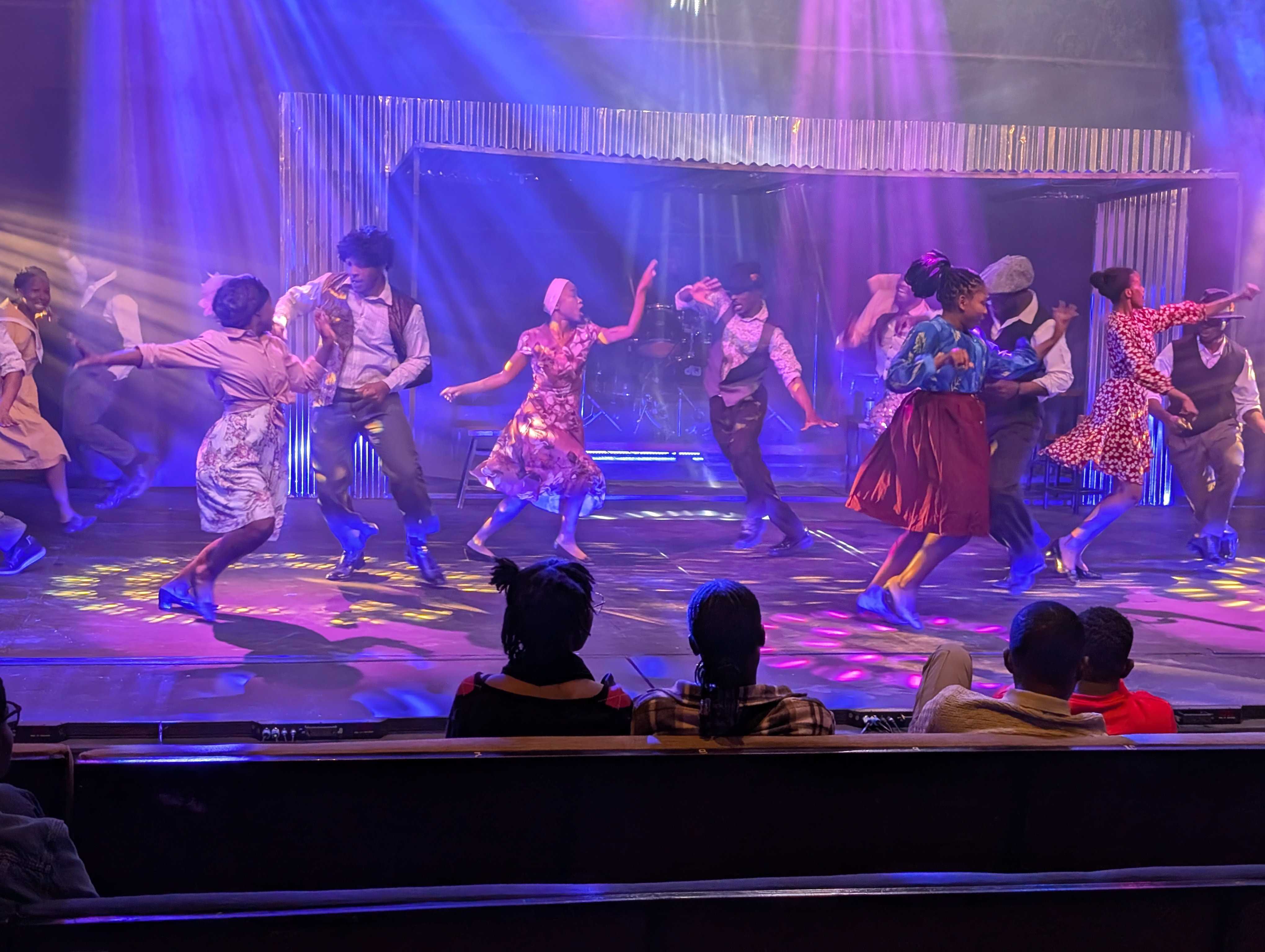 Male and female dancers in colorful costumes dancing underneath bright lights
